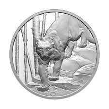 Engraved cougar stalking forward, head facing viewer, among trees and rocks in a circular design.